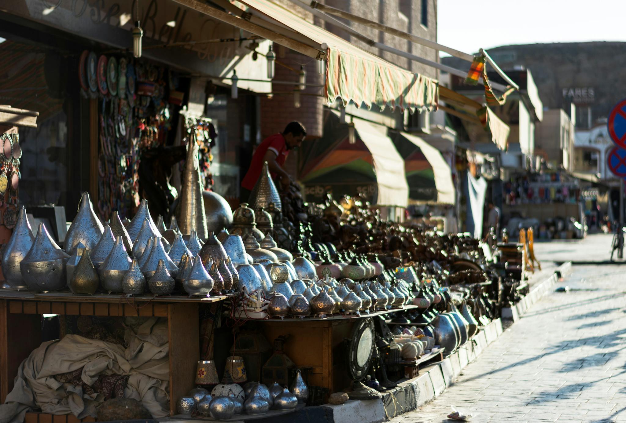 A lively outdoor market showcasing traditional metal crafts and vibrant textiles under the sunny sky.